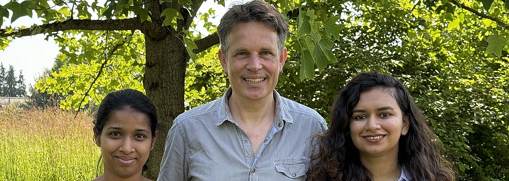 Ein Porträt von Krishani Tennakoon, Rob Roelfsema und Namrah Ahmad vor einem Baum im Botanischen Garten.